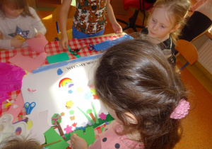 Dzieci dekorują plakat, wycinają i naklejają kolorowe elementy z papieru.